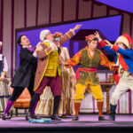 Multiple people posing together on stage with backdrops, dressed for the Barber of Seville performance.